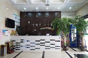 A reception desk with a digital screen, a wall-mounted TV, and potted plants.