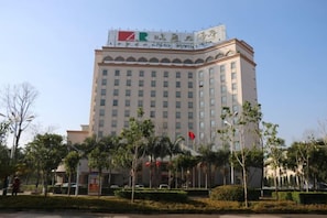 Un hotel de varios pisos con una bandera destacada en el techo, rodeado de jardines cuidados y un cielo despejado.