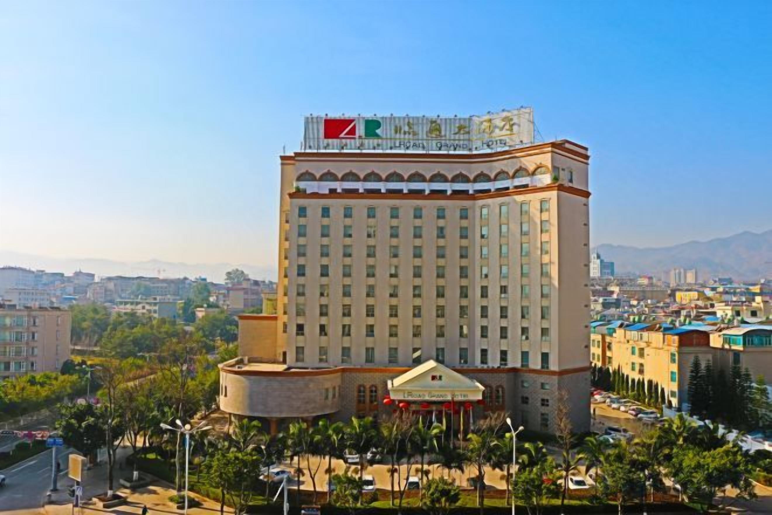 Hotel alto com uma bandeira grande no topo, cercado por um horizonte urbano e áreas verdes.