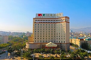 Un hotel moderno de gran altura con una bandera destacada en la cima, rodeado por un paisaje urbano y vegetación.