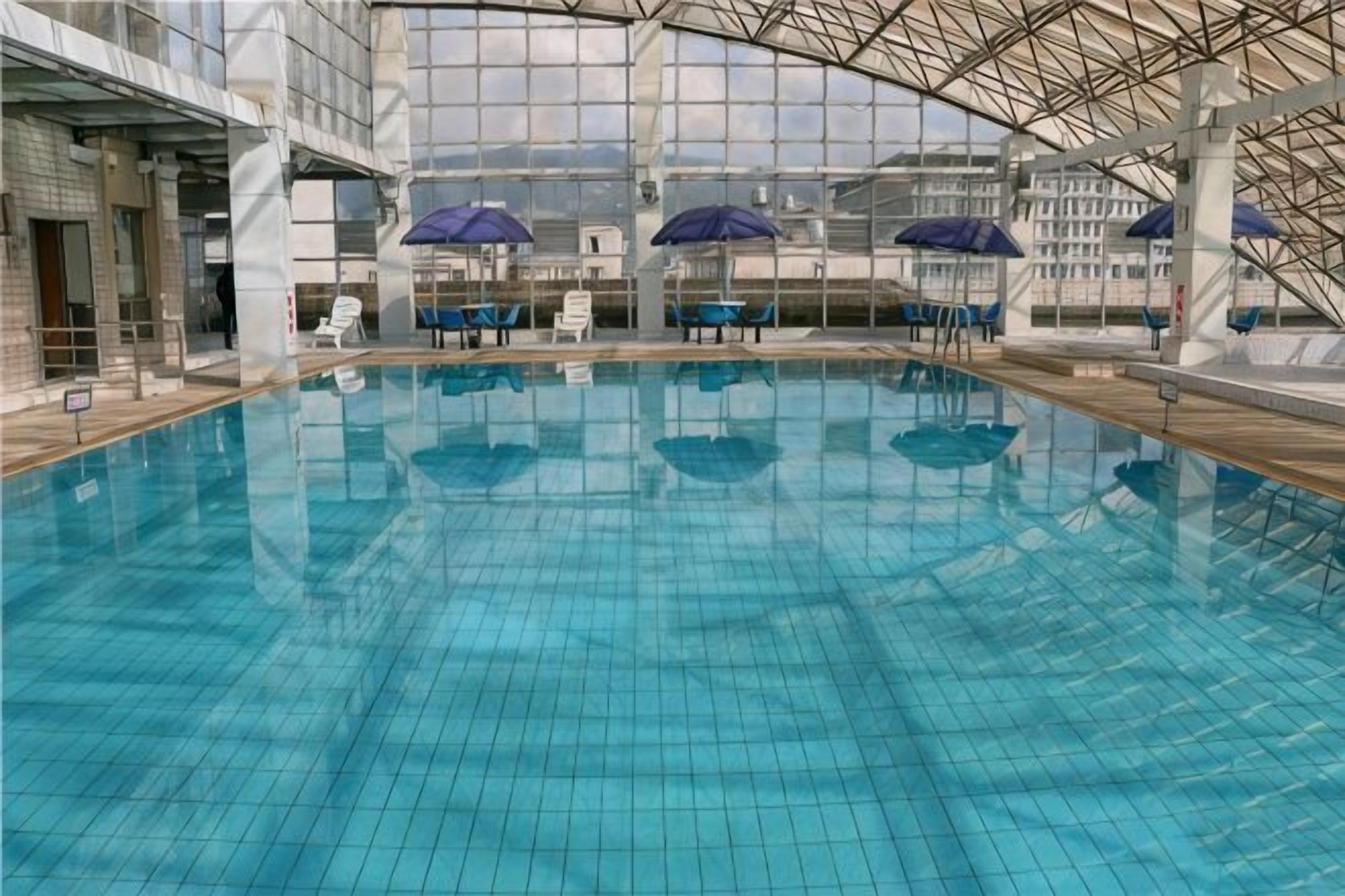 Piscina interior com paredes e teto azulejados, rodeada por espreguiçadeiras e guarda-sóis.
