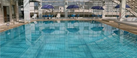 An indoor swimming pool with tiled walls and ceiling, surrounded by lounge chairs and umbrellas.