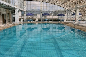 Una piscina interior con paredes y techo con azulejos, rodeada de sillas de descanso y sombrillas.