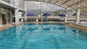 An indoor swimming pool with clear water, surrounded by lounge chairs and umbrellas. - L. Road Grand Hotel (Lincang)