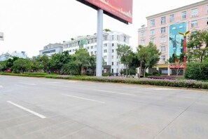 A wide street with buildings, trees, and a clear sky. - L. Road Grand Hotel (Lincang)