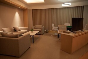 A modern hotel room with a sofa, armchairs, a desk, and a television.