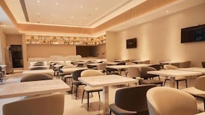 A modern hotel dining area with multiple tables and chairs, a central seating area, and a wall-mounted television. - Crown Hotel Junyue (Fuzhou)