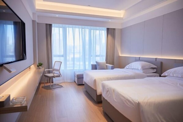 A modern hotel room with two beds, a desk with a chair, and a large window with curtains.