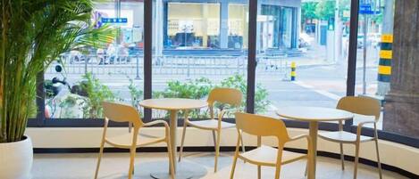 A seating area with tables and chairs, a large window with a view of a street and a Samsung store, and a potted plant.