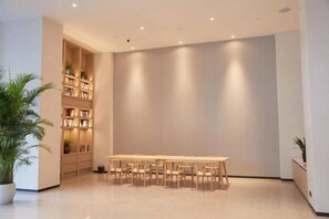 A modern interior with a long wooden table and chairs, a bookshelf, and potted plants. - Crown Hotel Junyue (Fuzhou)