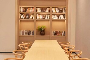 A conference room with a long table and chairs, surrounded by bookshelves filled with books and a vase with flowers. - Crown Hotel Junyue (Fuzhou)