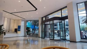 A modern lobby with a reception desk, glass doors leading to a Samsung store, and a polished floor. - Crown Hotel Junyue (Fuzhou)