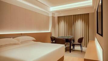 A hotel room with a bed, a desk, two chairs, and a large window with curtains.