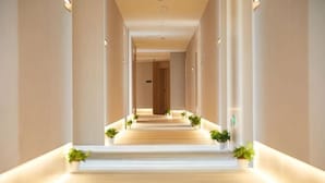 A long, well-lit corridor with a carpeted floor, flanked by columns and potted plants. - Crown Hotel Junyue (Fuzhou)