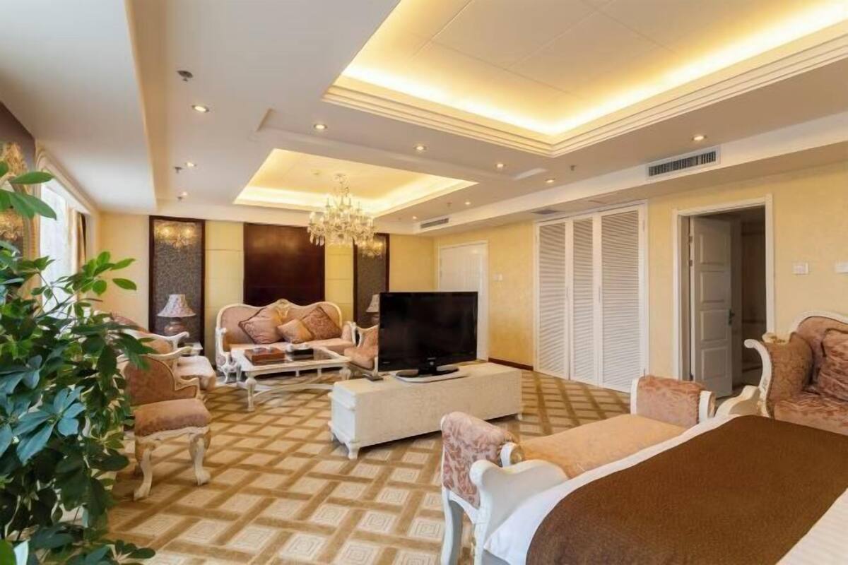 Una habitación de hotel con una cama grande, televisión, sofá, mesa de centro y candelabro.