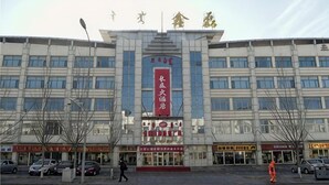 A multi-story building with a prominent red banner, multiple storefronts, and parked cars. - Changtai Palace Hotel (Hanggin Banner)