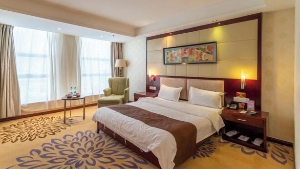 A hotel room with a large bed, a nightstand, a chair, and a window with curtains.
