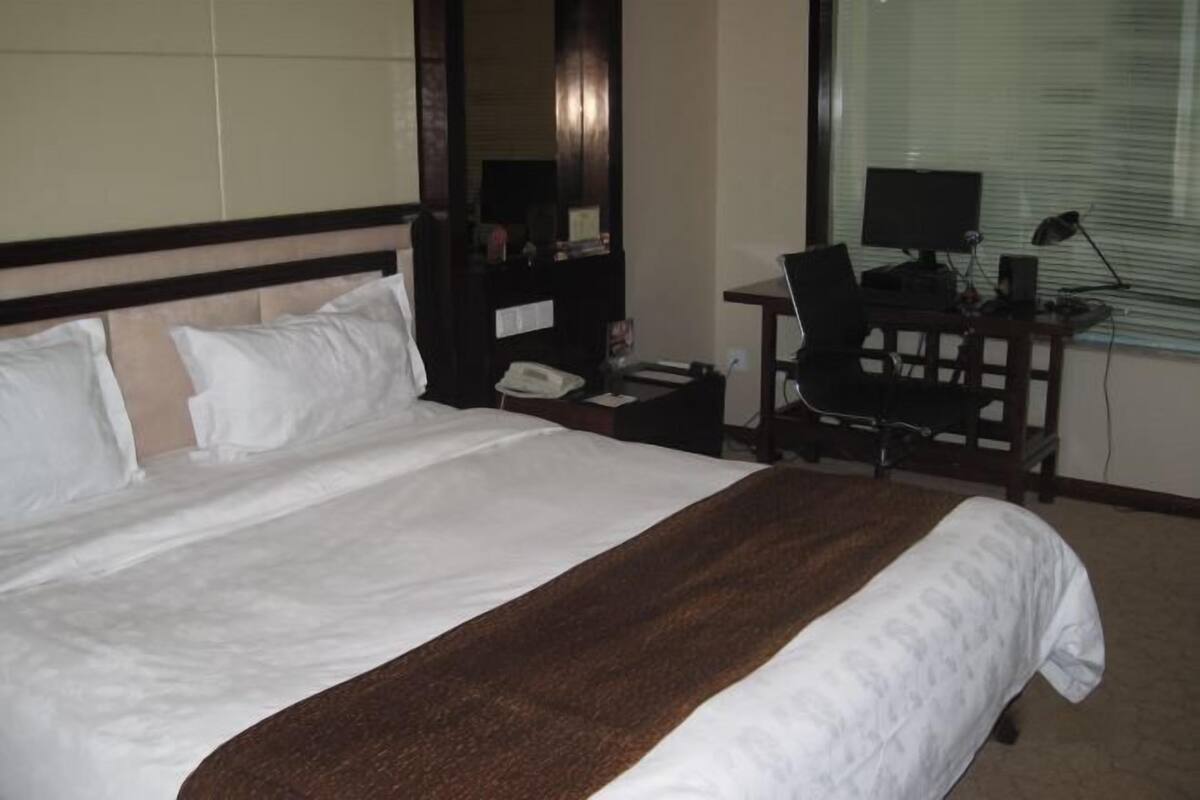Habitación de hotel con cama, escritorio con computadora, teléfono y ventana con persianas.