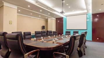 A conference room with a long table, multiple chairs, a projector screen, and a whiteboard.