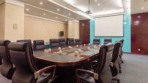 A conference room with a long table, multiple chairs, a projector screen, and a speaker.