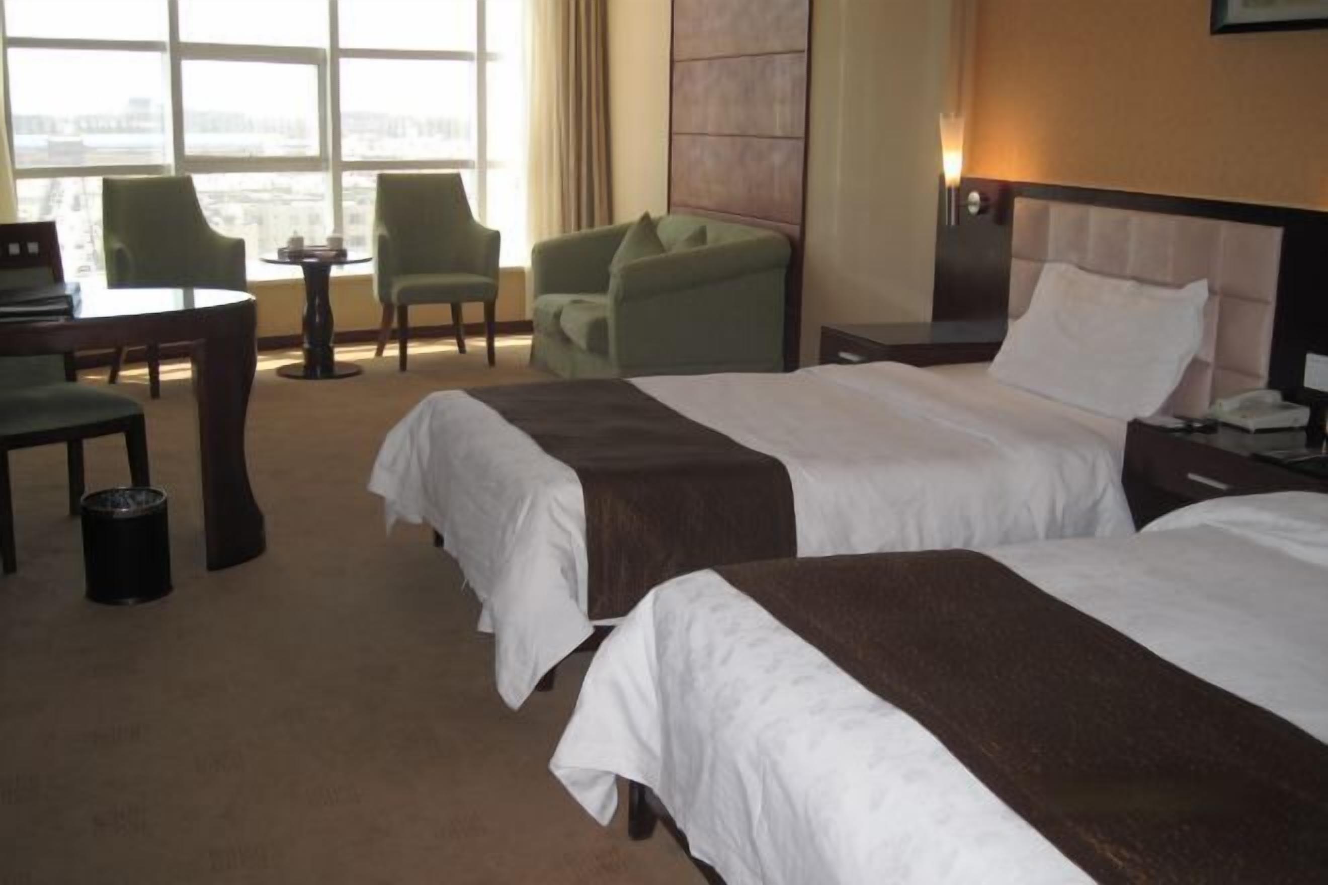 A hotel room with two beds, a desk, chairs, and a view of the city.