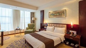 A hotel room with a large bed, a green armchair, a small table with a lamp, and a painting on the wall. - Changtai Palace Hotel (Hanggin Banner)