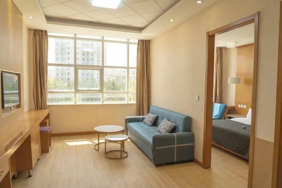 A hotel room with a large window, a blue sofa, a small round table, and a bed.