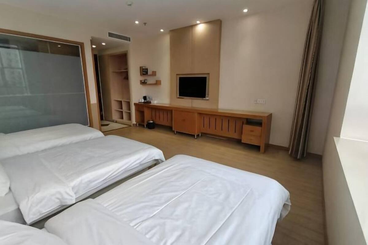 A hotel room with two beds, a TV, a wooden cabinet, and a mirror.