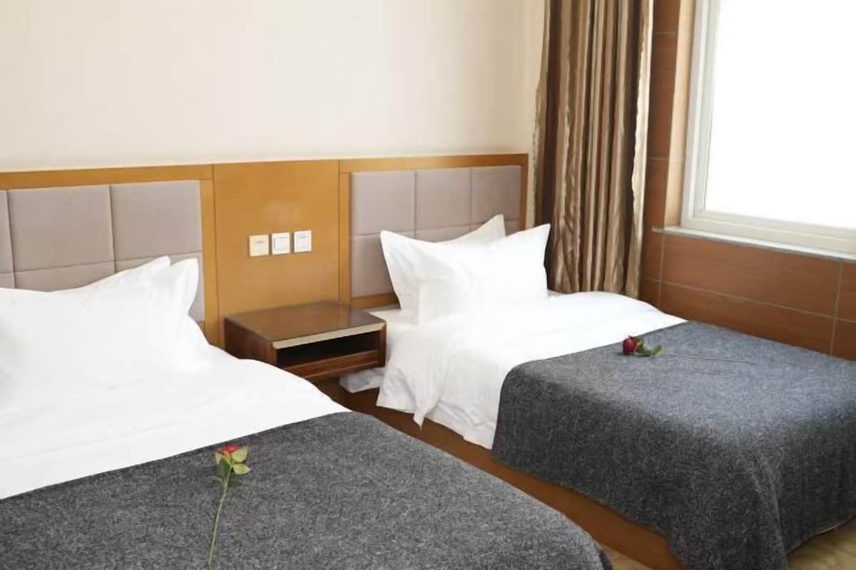 A hotel room with two beds, a nightstand, and a window with curtains.