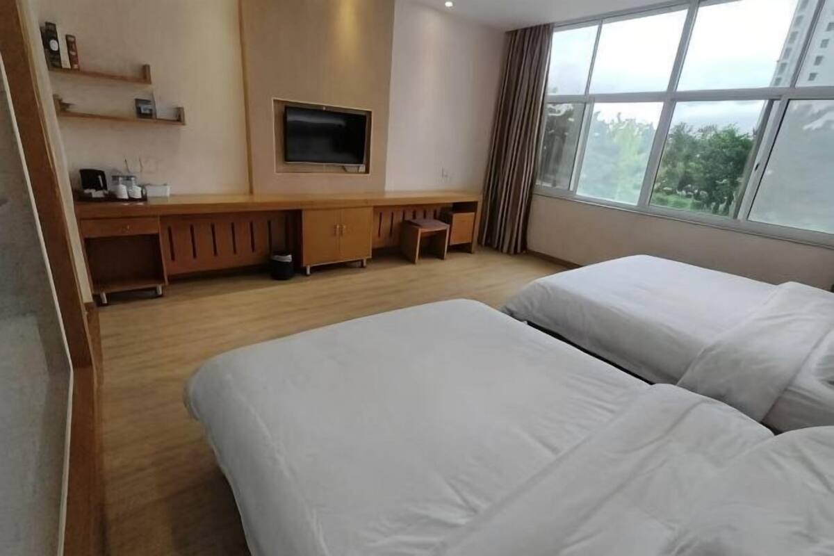 A hotel room with two beds, a TV, a desk, and a view of the outdoors.