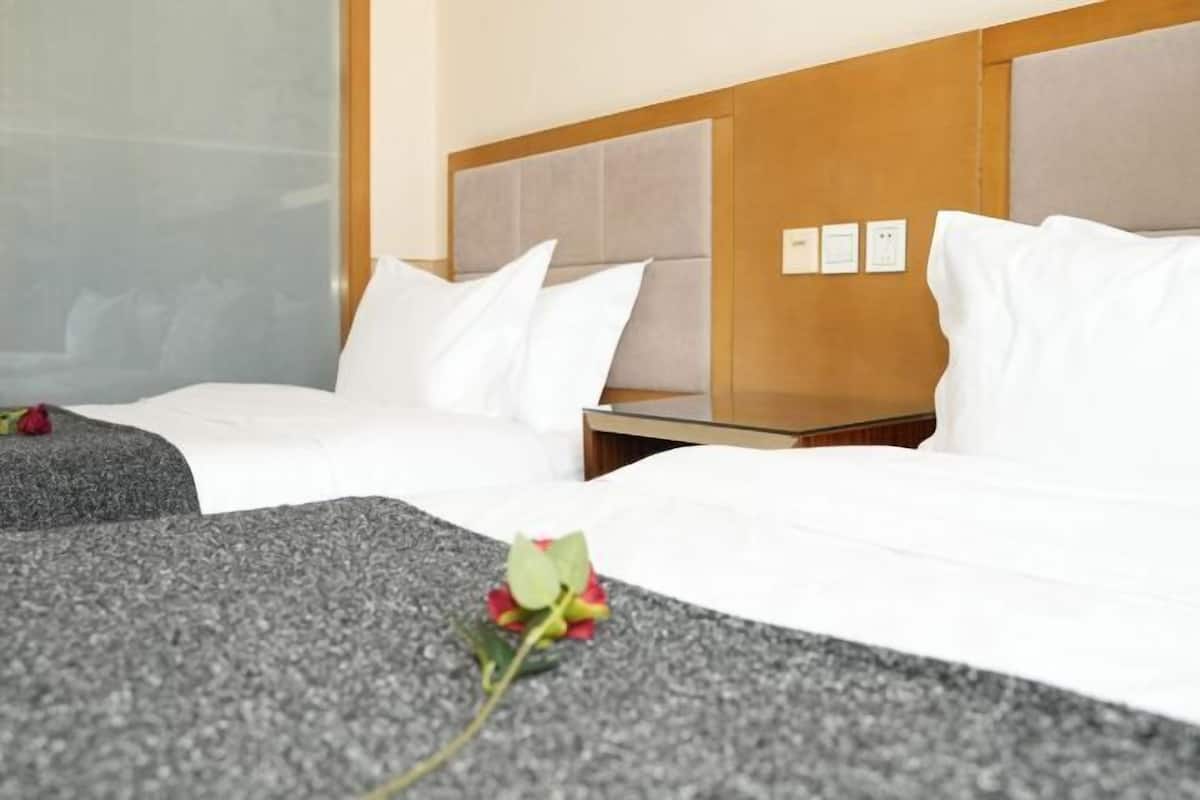 A hotel room with two beds, a wooden headboard, a small table, and a window.