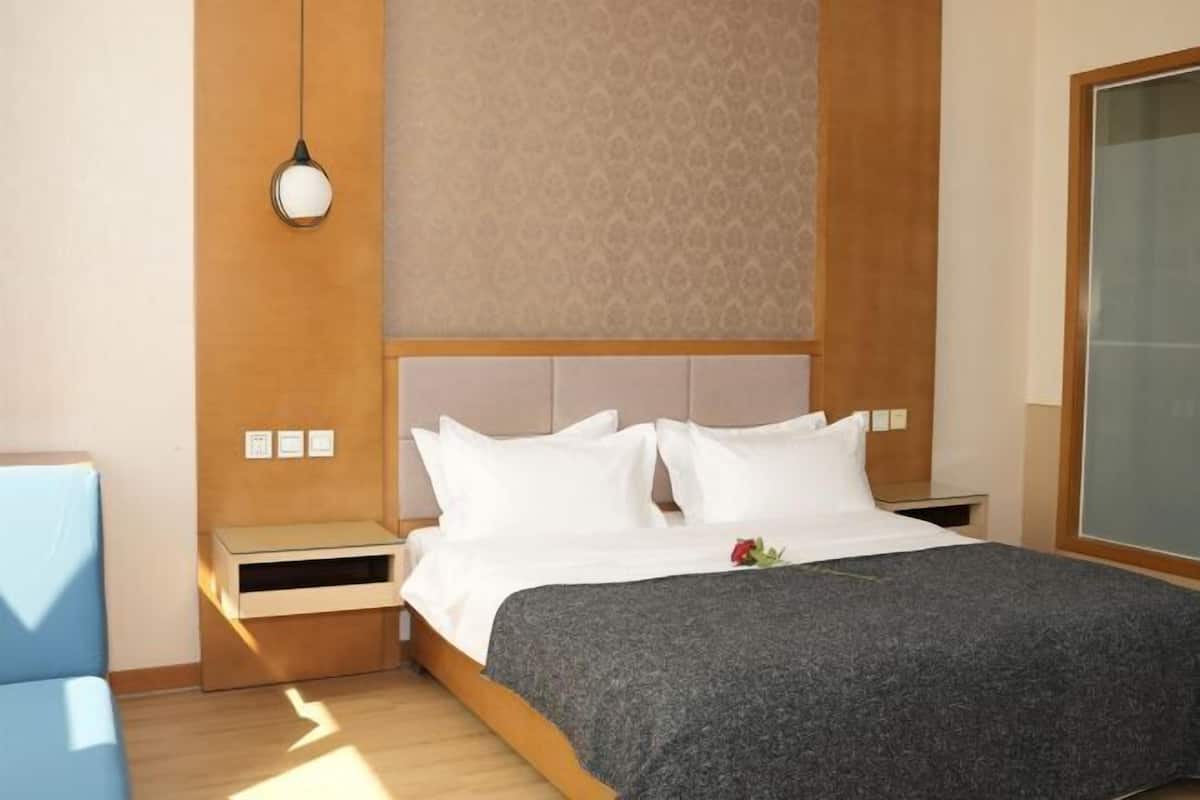 A hotel room with a bed, bedside tables, a nightstand, a wall-mounted light fixture, and a large window.