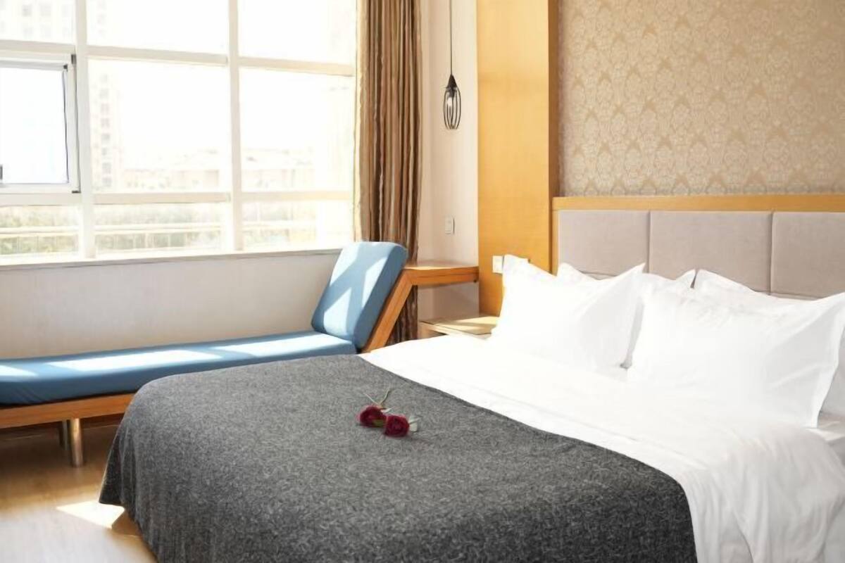 A hotel room with a bed, a seating area, and a window with curtains.