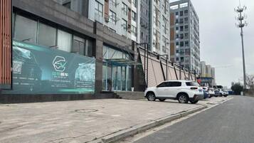 A multi-story building with a modern facade, a covered entrance, and a row of parked cars along the street.