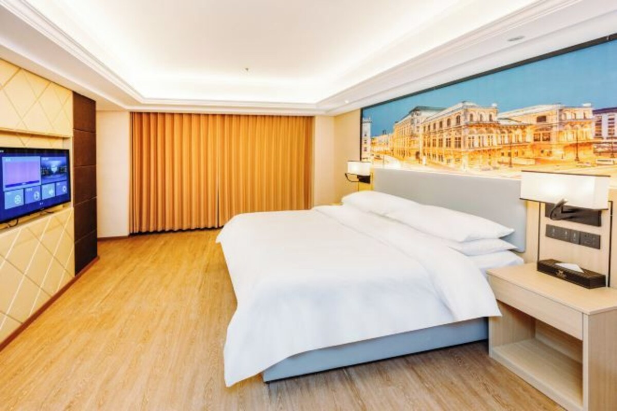 A hotel room with a bed, a TV, a painting of a cityscape, and a wooden floor.