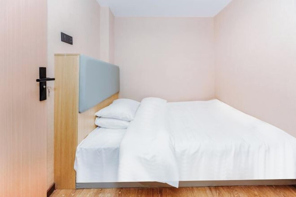 A single bed with white bedding in a room with light pink walls and a wooden floor.