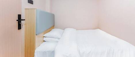 A single bed with white bedding in a room with light pink walls and a wooden floor.