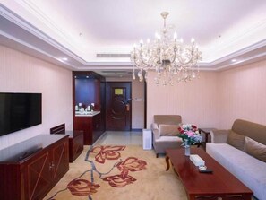A hotel room with a television, a sofa, a coffee table, a chandelier, and a carpet with a floral pattern. - Vienna International Hotel (Yangzhou)