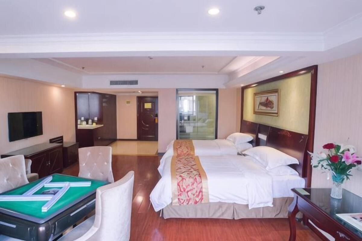 A hotel room with a bed, a desk with a chair, a television, and a bathroom visible through an open door.