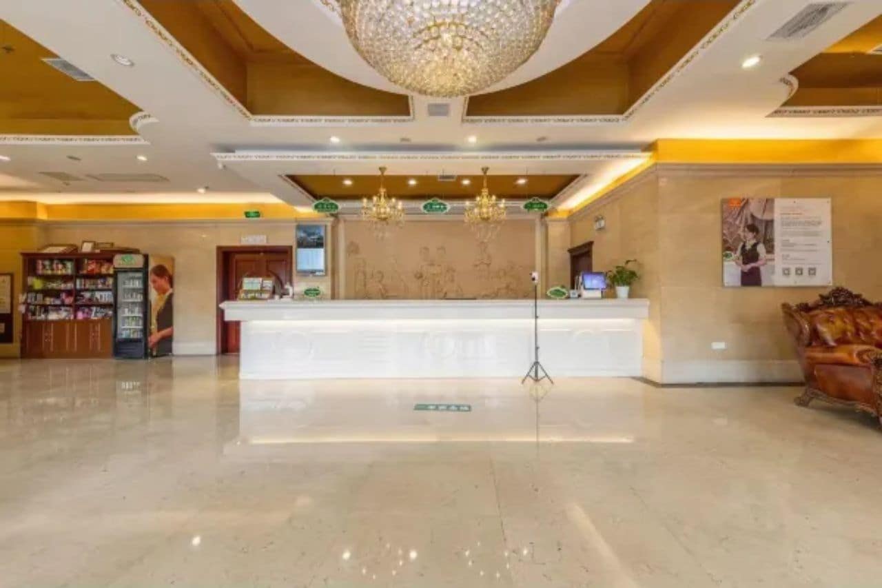 A hotel lobby with a reception desk, a chandelier, a vending machine, and a plush armchair.