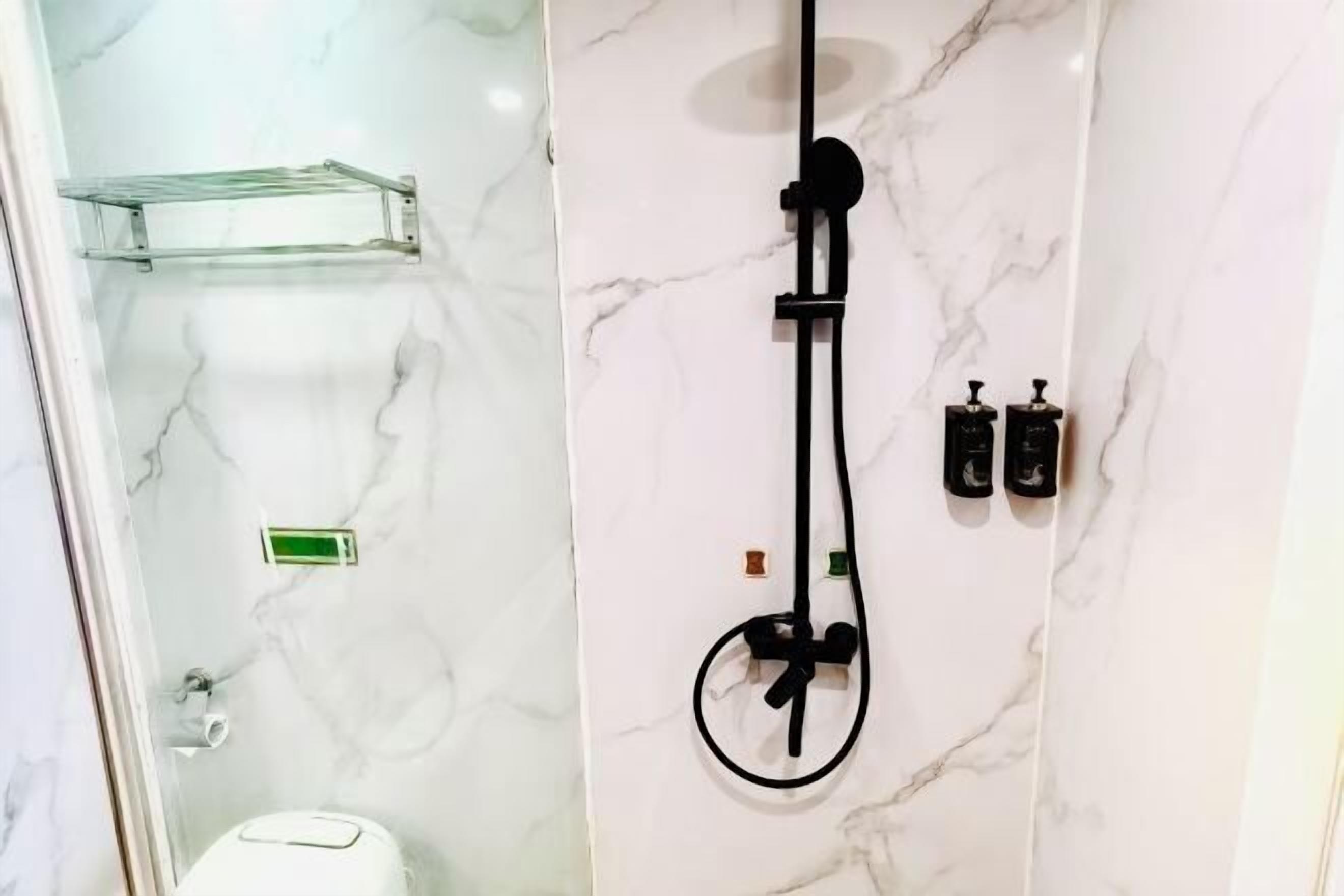 A bathroom with a glass shower enclosure, a toilet, and a marble wall.