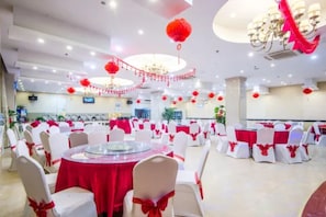 Una sala da banchetti con tavoli rotondi, sedie bianche con nastri rossi e lanterne rosse.