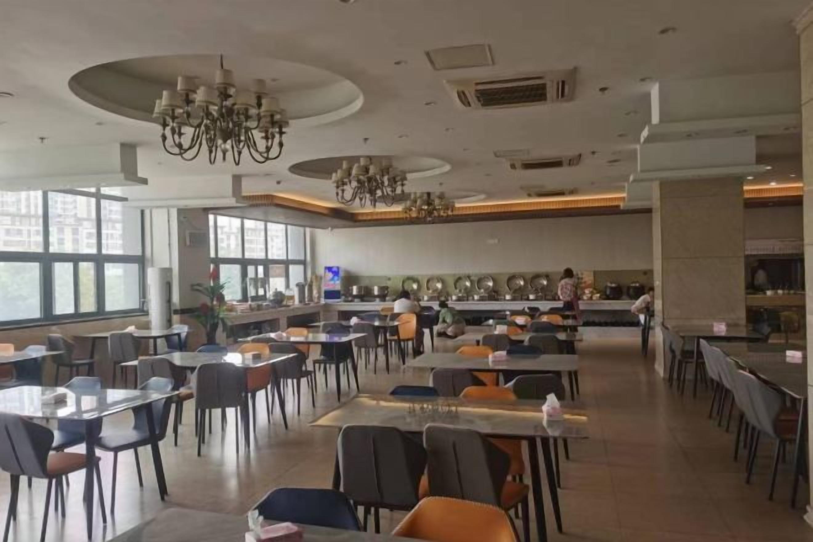 A spacious dining area with multiple tables and chairs, large windows, and a kitchen area in the background.