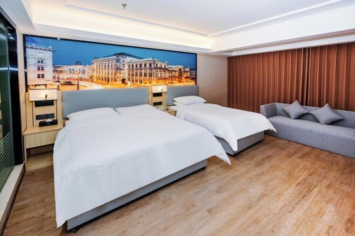 A hotel room with two beds, a sofa, a large window with a cityscape view, and a wooden floor.