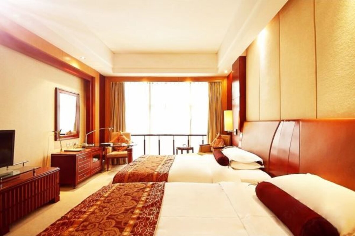 A hotel room with two beds, a desk, a TV, and a large window.