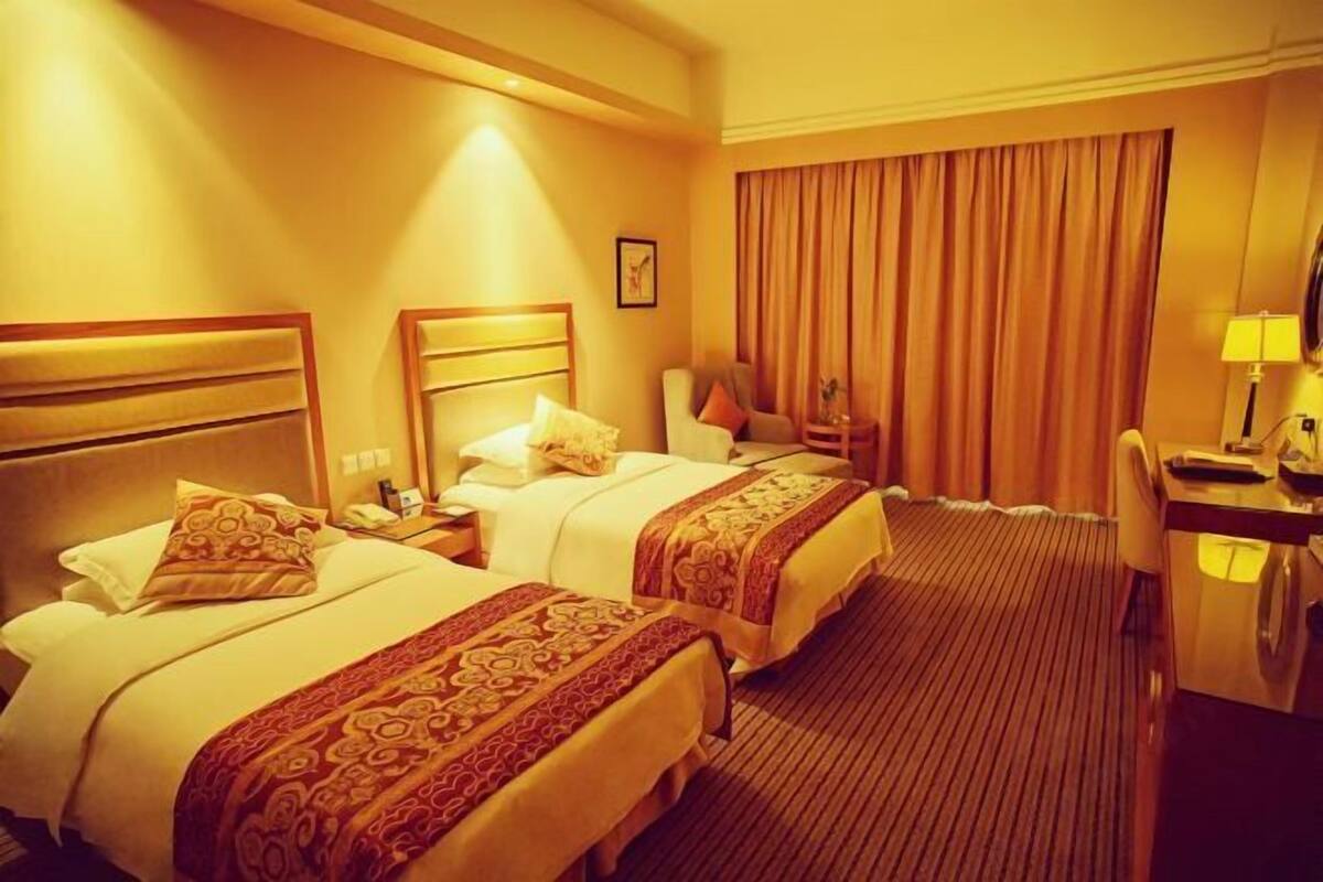 A hotel room with two beds, a desk, a chair, and a large window with curtains.