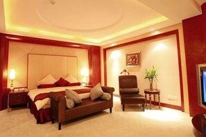 Ein Hotelzimmer mit einem großen Bett, einer Couch, einem kleinen Tisch, einem Sessel und einem Fernseher.