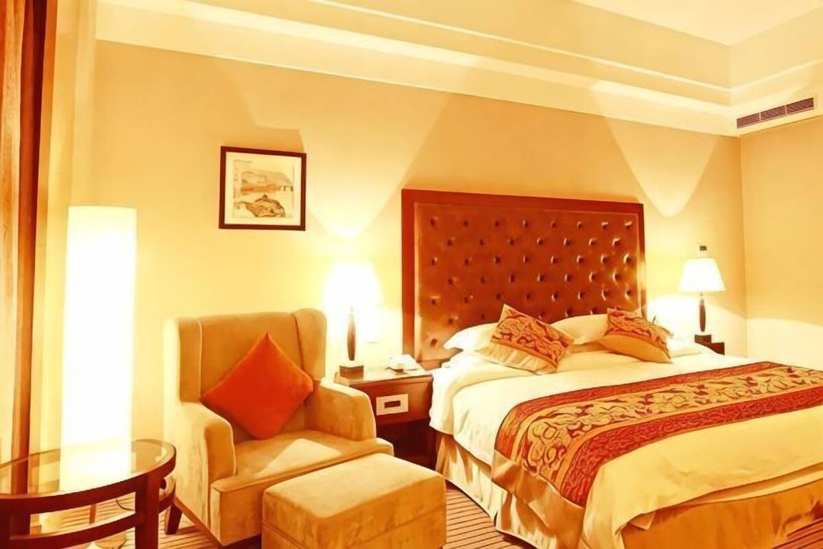 A hotel room with a large bed, a chair, a nightstand, and a lamp.
