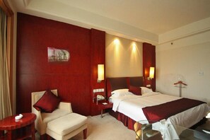 A hotel room with a large bed, a bedside table, a chair, and a desk.