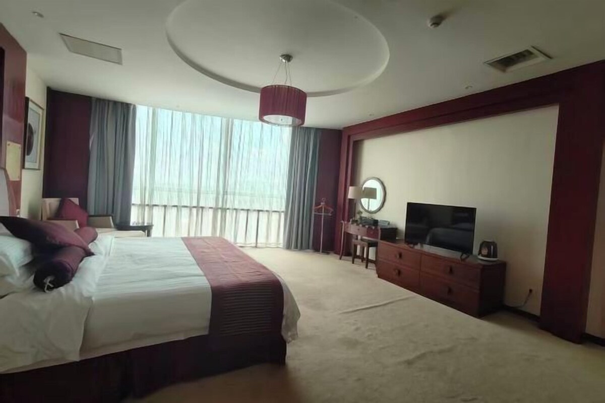 Quarto de hotel com uma cama grande, televisão, escrivaninha com cadeira e janela com cortinas.